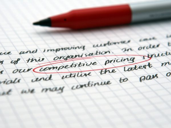 Papier met handgeschreven tekst en rode pen, met "competitive pricing" omcirkeld, symboliserend prijsstrategie en zakelijke documentatie.