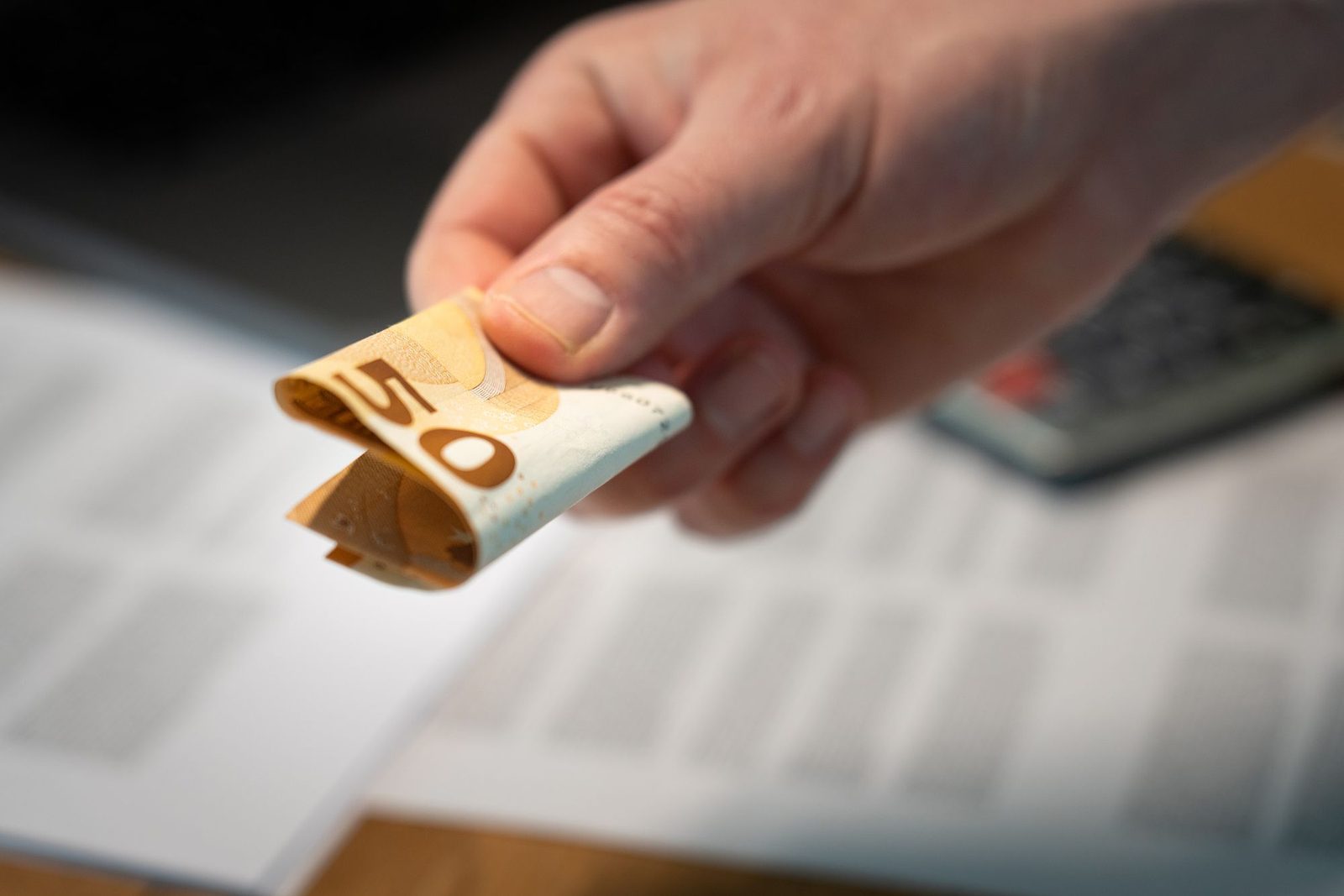 Hand met een briefje van 50 euro boven papieren en een rekenmachine: een teruggeboekte incasso alsnog voldoen